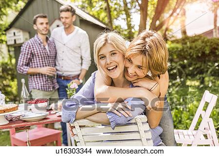 Picture - "Group of friends at garden party, two female friends embracing". Fotosearch