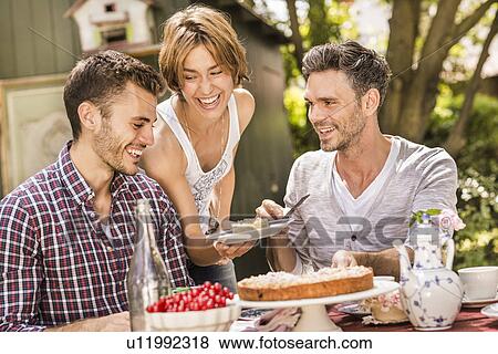 Stock Photo - "Group of friends enjoying garden party, young woman holding plate with dessert". Fotosearch