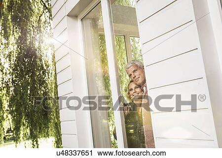 Stock Image - Husband and wife looking out of window into garden. Fotosearch