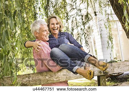 Stock Image - Husband carrying wife onto garden fence. Fotosearch