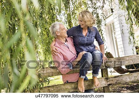 Stock Photography - Husband carrying wife onto garden fence. Fotosearch