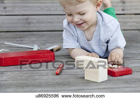 Stock Photograph - Male toddler playing with wooden blocks for toy boat on pier. Fotosearch