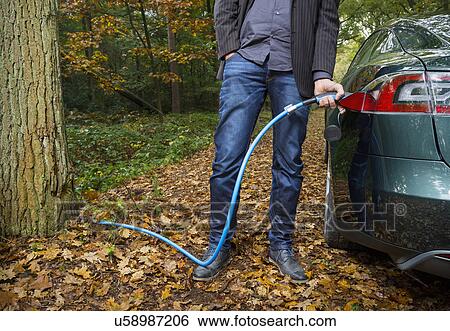 Stock Photograph - Man charging electric car in forest. Fotosearch