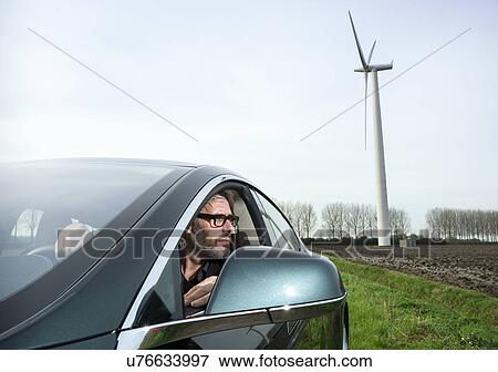 Stock Photo - Man in car with wind turbine in background. Fotosearch