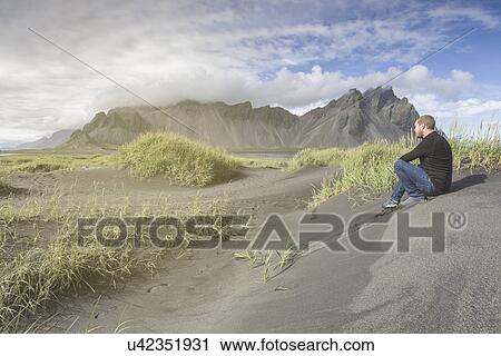 Stock Image - "Man sitting in sand dune, Stokksnes, Iceland". Fotosearch