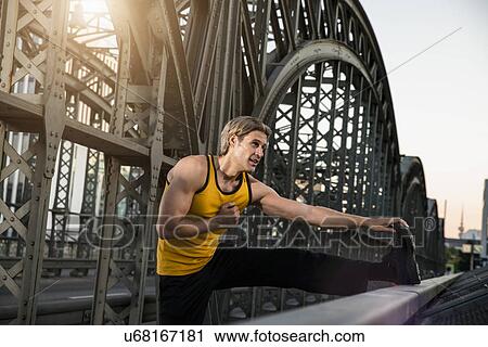 Stock Image - "Man stretching leg on bridge, Munich, Bavaria, Germany". Fotosearch