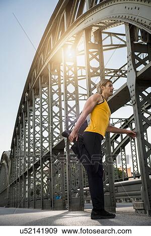 Stock Photo - "Man stretching leg on bridge, Munich, Bavaria, Germany". Fotosearch