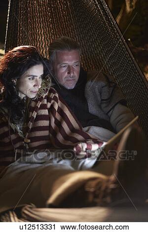 Mature hippy couple in garden hammock at night looking at digital tablet View Large Photo Image Stock Image - Mature hippy couple in garden hammock at night looking at digital tablet. Fotosearch
