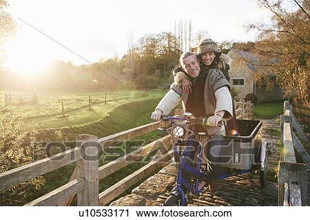Stock Image - Mature hippy couple on tricycle and trailer on rural road. Fotosearch