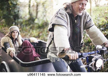 Stock Photography - Mature hippy couple riding tricycle and trailer on rural road. Fotosearch