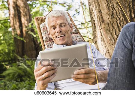 Mature man using digital tablet on hammock View Large Photo Image Stock Photography - Mature man using digital tablet on hammock. Fotosearch