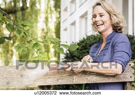 Stock Image - Mature woman playing with hosepipe in garden. Fotosearch