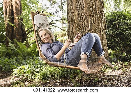 Stock Image - Mature woman relaxing with bowl of cherries on hammock. Fotosearch