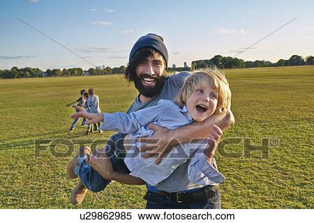 Mid adult man carrying son in field View Large Photo Image Stock Photography - Mid adult man carrying son in field. Fotosearch