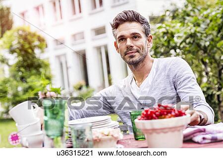 Mid adult man sitting at table in garden View Large Photo Image Stock Image - Mid adult man sitting at table in garden. Fotosearch