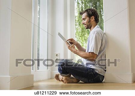 Mid adult man using touchscreen on digital tablet in sitting room View Large Photo Image Stock Photo - Mid adult man using touchscreen on digital tablet in sitting room. Fotosearch
