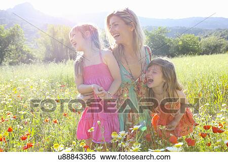 Stock Photography - "Mid adult woman and two daughters laughing in wildflower meadow, Majorca, Spain". Fotosearch