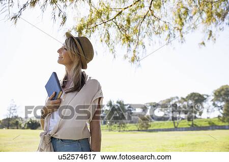Stock Photo - "Mid adult woman in field, holding book". Fotosearch