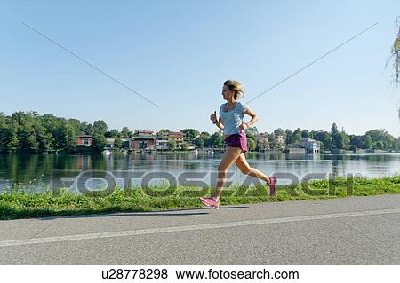 Mid adult woman running on road alongside lake View Large Photo Image Stock Photo - Mid adult woman running on road alongside lake. Fotosearch