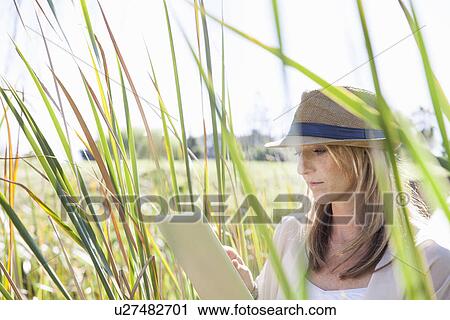 "Mid adult woman sitting in long grass, using digital tablet" View Large Photo Image Stock Image - "Mid adult woman sitting in long grass, using digital tablet". Fotosearch