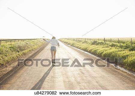 Stock Image - "Mid adult woman walking down country road, rear view". Fotosearch