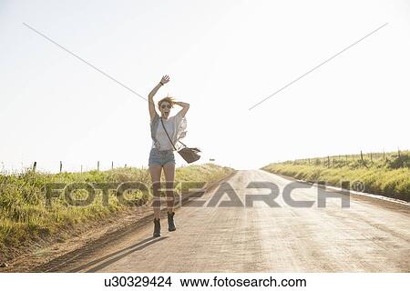 Picture - "Mid adult woman walking on country road, waving arms in air". Fotosearch