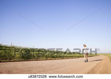 Stock Photo - "Mid adult woman walking on country road, looking at mobile phone". Fotosearch