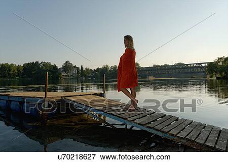 Stock Photo - "Mid adult woman wrapped in towel, walking on jetty". Fotosearch
