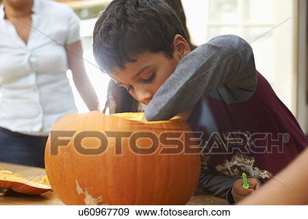 Stock Photo - Mother and children hollowing out pumpkin in dining room. Fotosearch