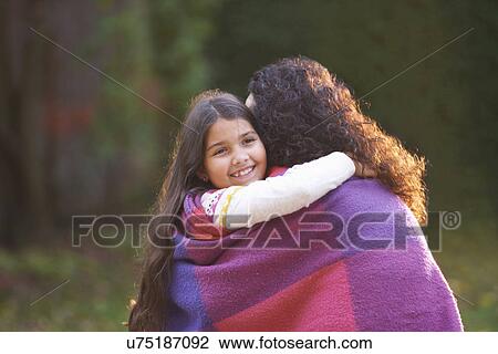 Stock Image - Mother and daughter wrapped in blanket in garden. Fotosearch