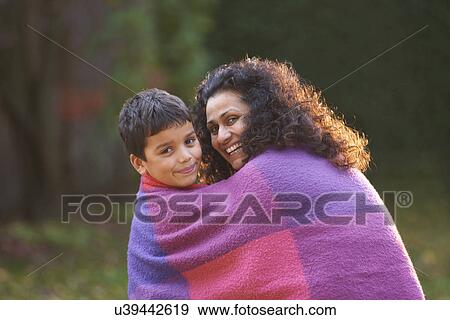 Stock Photo - Mother and son wrapped in blanket in garden. Fotosearch