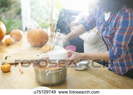 Stock Photo - Mother serving pumpkin soup for daughter in kitchen. Fotosearch