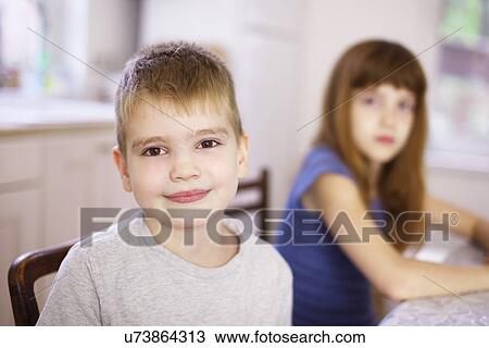 Stock Image - Portrait of boy with sister at kitchen table. Fotosearch