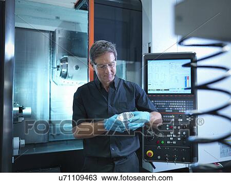 Stock Image - Portrait of engineer holding engineered component at CNC machine in factory. Fotosearch
