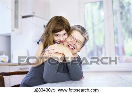 Stock Photography - Portrait of girl hugging grandmother at kitchen table. Fotosearch