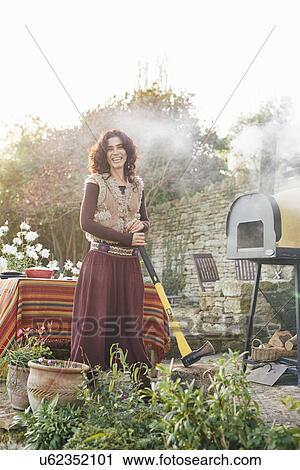Stock Image - Portrait of mature hippy female with axe in garden. Fotosearch