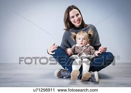 Stock Image - Portrait of mid adult woman sitting on floor with toddler daughter sitting on lap. Fotosearch