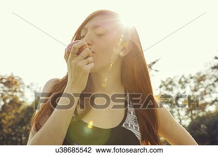 Portrait of red haired young woman eating apple in park View Large Photo Image Stock Image - Portrait of red haired young woman eating apple in park. Fotosearch
