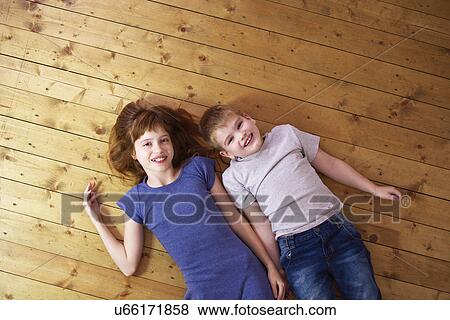 Stock Photo - Portrait of sister and brother lying on wooden floorboards. Fotosearch