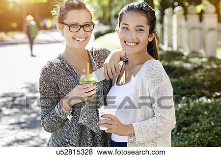 Stock Photo - Portrait of two young female friends in park drinking takeaway coffee. Fotosearch
