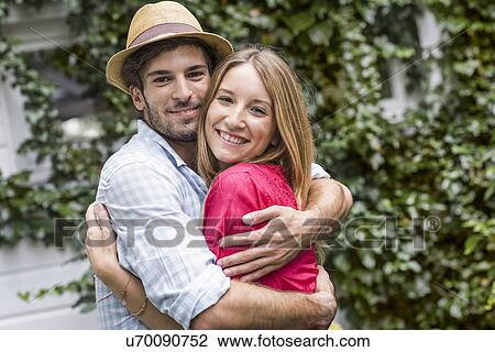 Stock Image - Portrait of young couple hugging in garden. Fotosearch