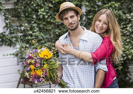 Portrait of young couple with bunch of flowers hugging in garden View Large Photo Image Stock Image - Portrait of young couple with bunch of flowers hugging in garden. Fotosearch