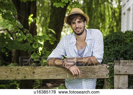 Portrait of young man leaning against wooden fence View Large Photo Image Stock Photo - Portrait of young man leaning against wooden fence. Fotosearch
