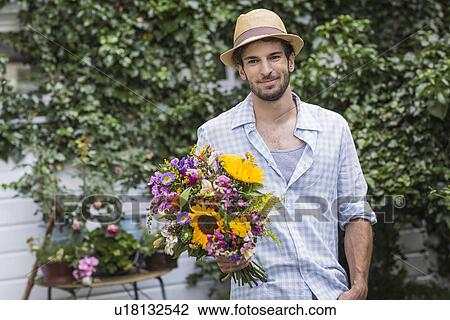 Stock Image - Portrait of young man with bunch of flowers in garden. Fotosearch