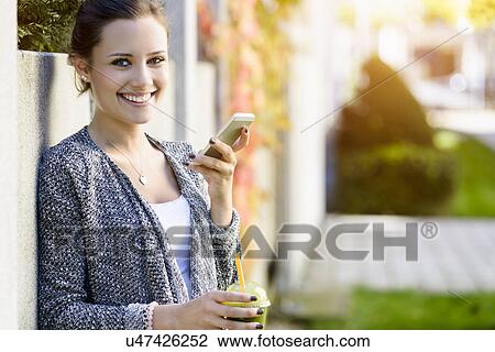 Portrait of young woman leaning against park wall using smartphone View Large Photo Image Stock Image - Portrait of young woman leaning against park wall using smartphone. Fotosearch