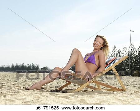Stock Photography - "Portrait of young woman posing on deck chair at beach, Altona, Melbourne, Victoria, Australia". Fotosearch