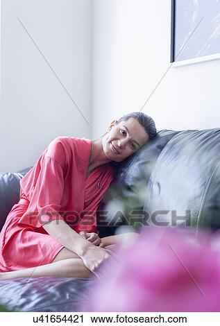 Portrait of young woman wearing bathrobe curled up on living room sofa View Large Photo Image Stock Image - Portrait of young woman wearing bathrobe curled up on living room sofa. Fotosearch
