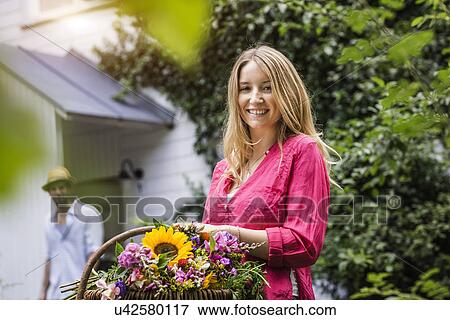 Stock Photo - Portrait of young woman with basket of flowers in garden. Fotosearch