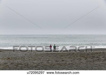 Stock Photo - "Rear view of brother and sister on black beach, Hvalnes, Iceland". Fotosearch