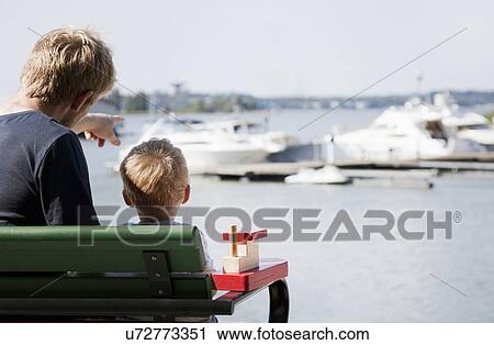 Stock Image - "Rear view of male toddler and father watching boats in harbor, Somerniemi, Finland". Fotosearch